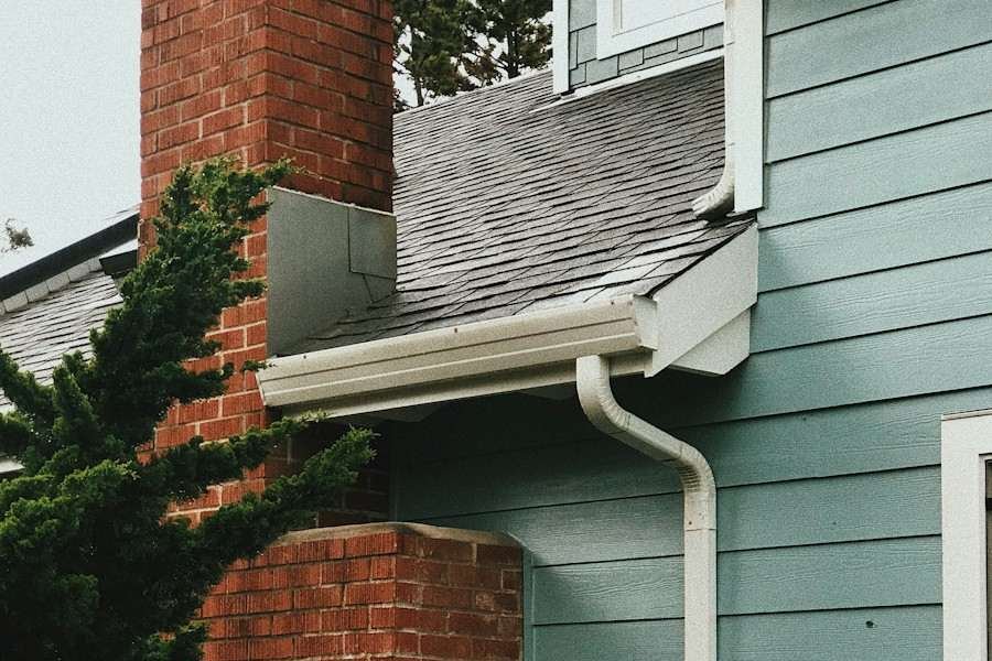 A shingle roof and gutter beside a brick chimney on a blue-sided house