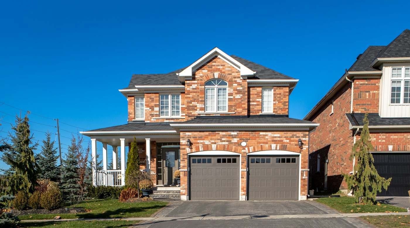 A brick two-story home with a front porch and a dark shingle roof