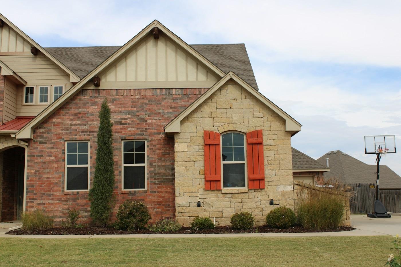 A brick and stone house with red shutters and an architectural shingle roof