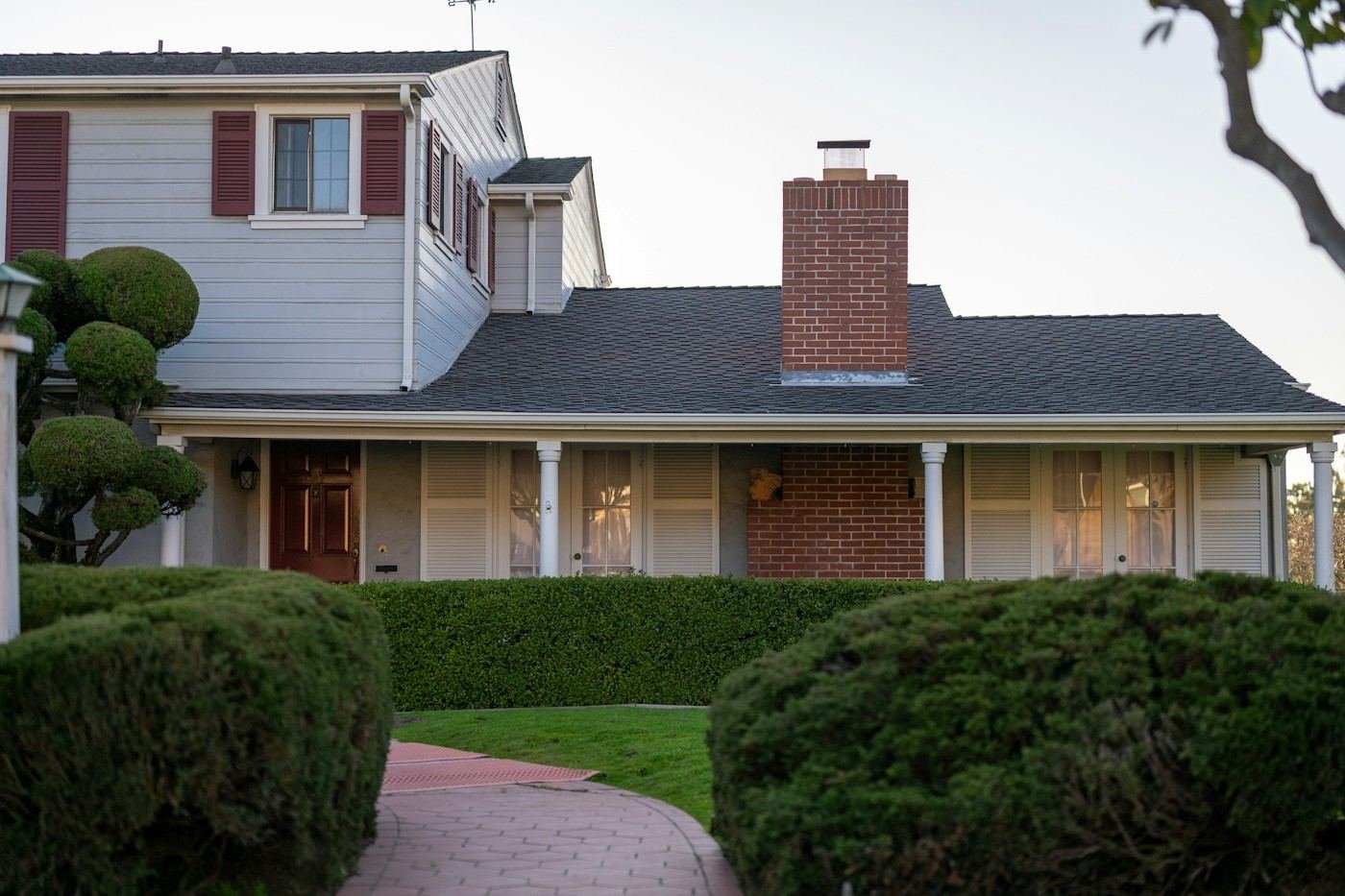 A house with red shutters, a brick chimney and a dark shingle roof