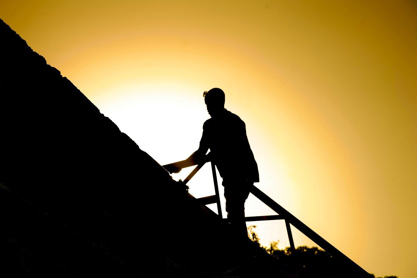 A roofer climbing a ladder onto a roof, outlined against the sun