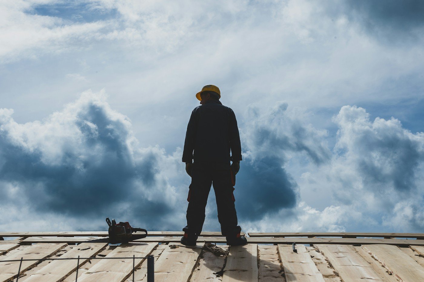 A roofer in a hard hat standing on a roof deck under building clouds