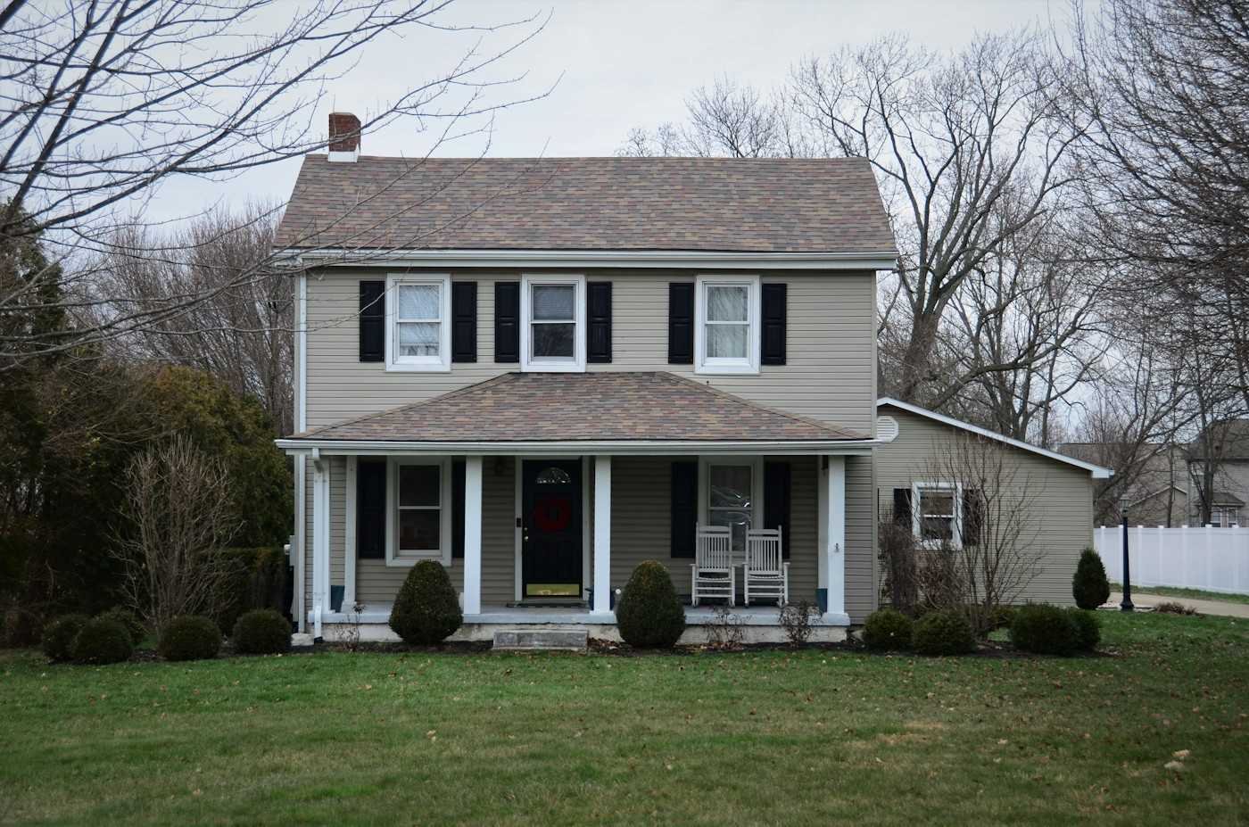 A two-story house with black shutters, a front porch and a brown shingle roof