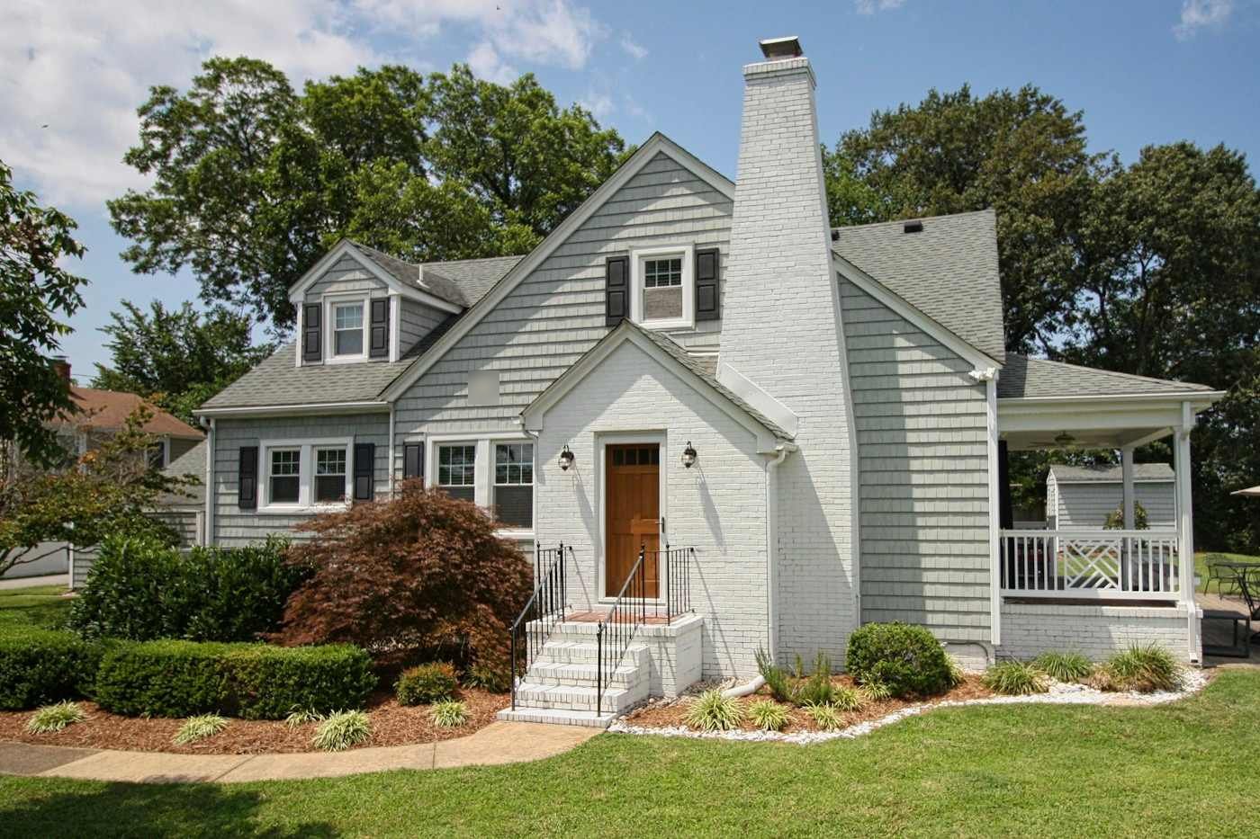 A white brick cape with a tall chimney and a gray shingle roof